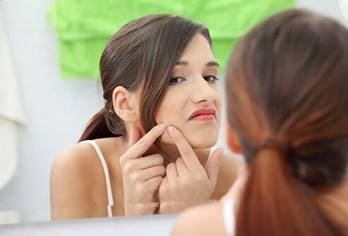 A teenage girl checks her skin in the mirror.