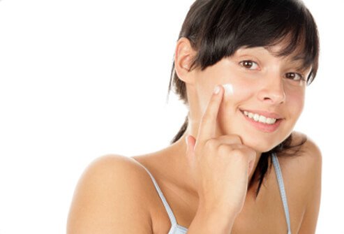 A teenage girl applies acne medication to her face.