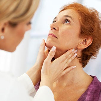 A doctor diagnosing a woman's swollen lymph nodes by examining her neck.
