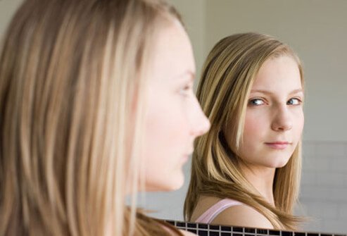 A teen girl looks in the mirror.