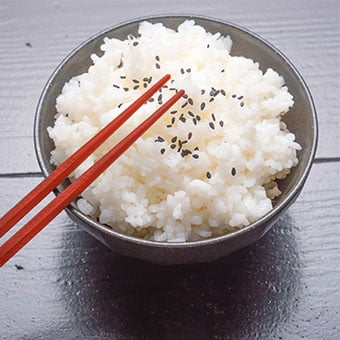 A bowl of white rice with chopsticks.