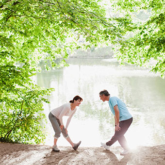 A couple stretches by a lake in the woods.