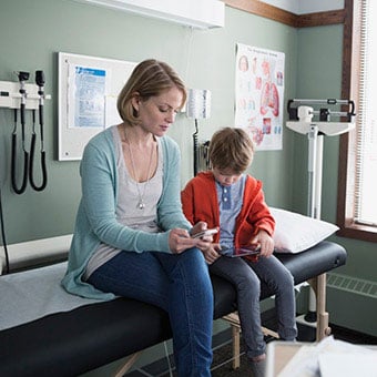 A mother and her son wait to see the doctor in the medical exam room.