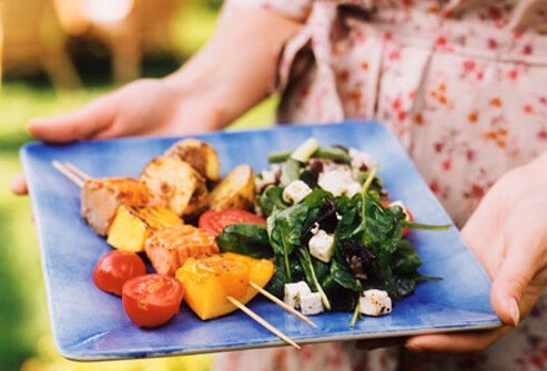 Woman holding a plate of barbecue food and salad.